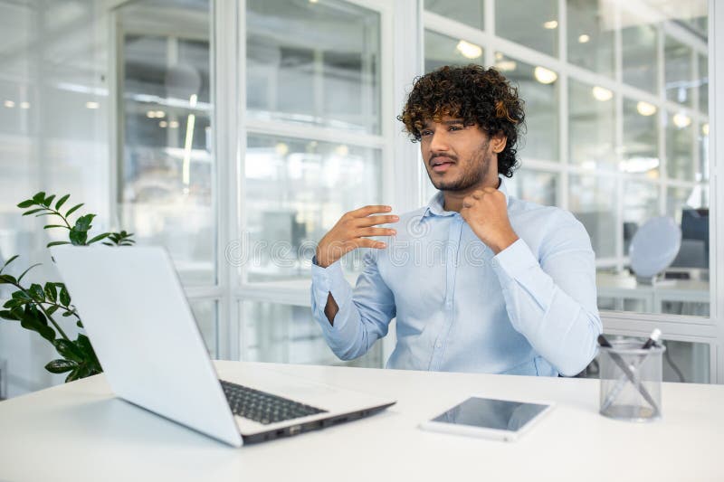 A young businessman loosens his tie, feeling hot and stressed in a bright, modern office setting. The heat seems too much as he cools himself with his hand. A young businessman loosens his tie, feeling hot and stressed in a bright, modern office setting. The heat seems too much as he cools himself with his hand.