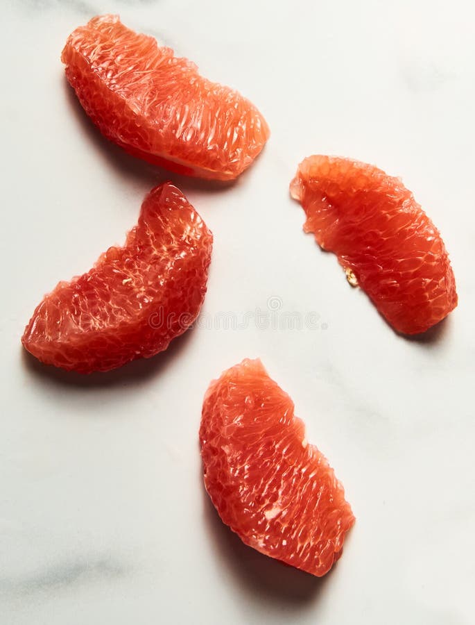 Peeled and sliced, divided in sections grapefruit on the white marble countertop. Bright, hey-key vertical photo. High quality photo. Peeled and sliced, divided in sections grapefruit on the white marble countertop. Bright, hey-key vertical photo. High quality photo