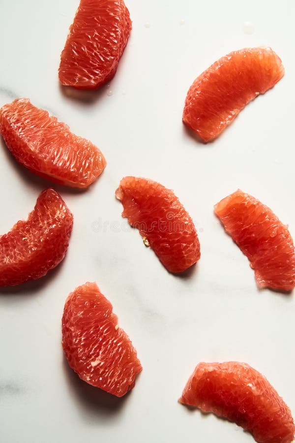 Peeled and sliced, divided in sections grapefruit on the white marble countertop. Bright, hey-key vertical photo. High quality photo. Peeled and sliced, divided in sections grapefruit on the white marble countertop. Bright, hey-key vertical photo. High quality photo