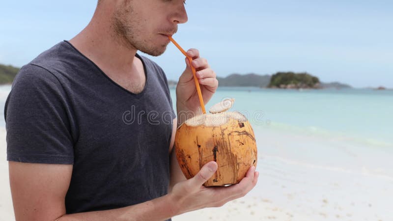 在白色沙滩上喝椰子的男子的特写