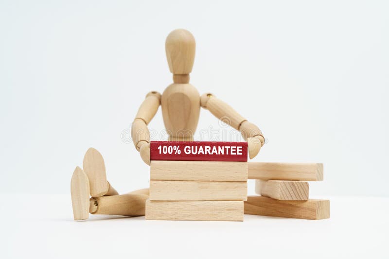 Business concept. On a white surface sits a wooden man in his hands a block with the inscription - 100 percent guarantee. Business concept. On a white surface sits a wooden man in his hands a block with the inscription - 100 percent guarantee