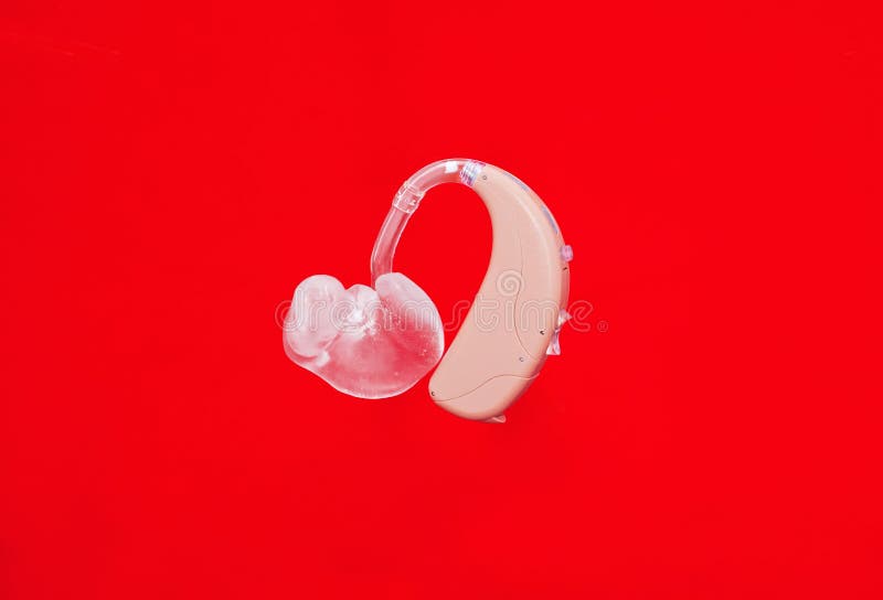 Hearing aid with earmold in front of a vivid red background. Hearing aid with earmold in front of a vivid red background