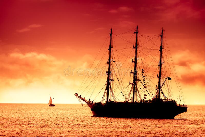 Large black tall ship on the high seas at dusk. Flying Dutchman at the amber red sunset. Large black tall ship on the high seas at dusk. Flying Dutchman at the amber red sunset