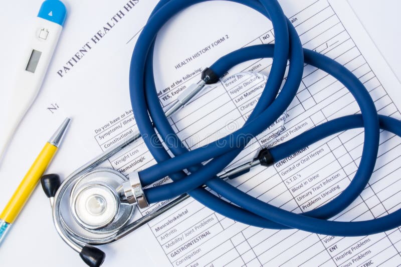 在纸上摆放着患者的健康史医疗问卷，以及医生的诊断工具——听诊器和体温计。初步检查和将患者收治入院的过程 免版税库存照片