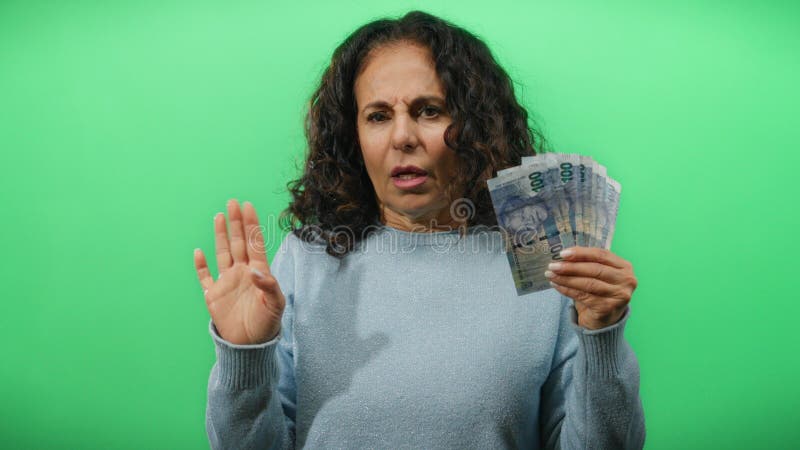 在绿色背景墙上，手持南非纸币的中年妇女惊讶地表情 免版税库存照片