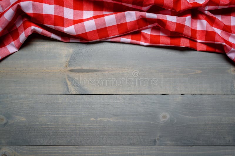 A gingham or checked picnic tablecloth on old wooden table top view. A gingham or checked picnic tablecloth on old wooden table top view