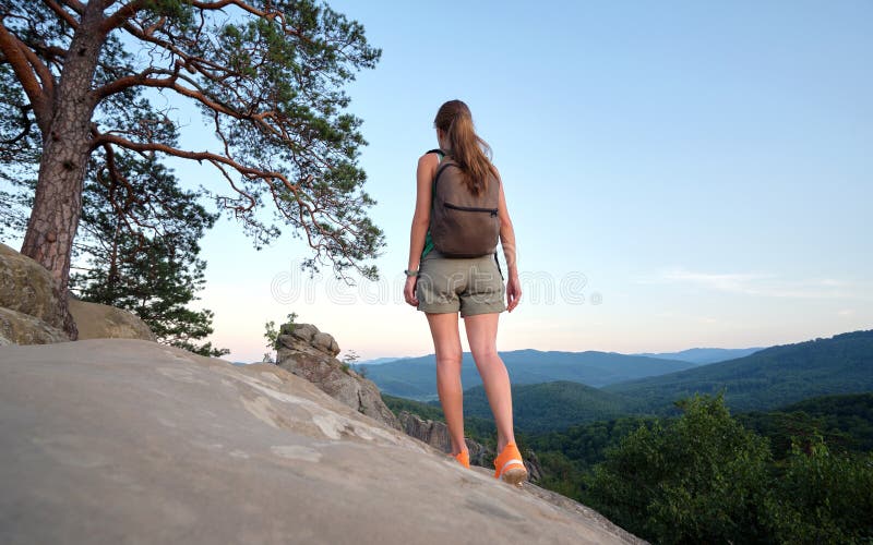 在荒野之路旅行时，徒步登山的女人站在山上的人行道上享受大自然. 孤独的女性旅行者 库存照片