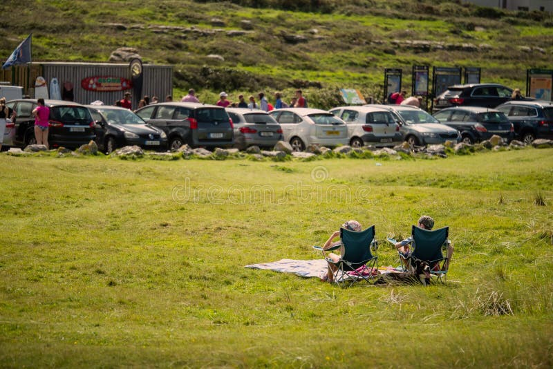 在阴凉的19天里，人们在前景一片草地上晒日光浴，在繁忙的停车场和冲浪店