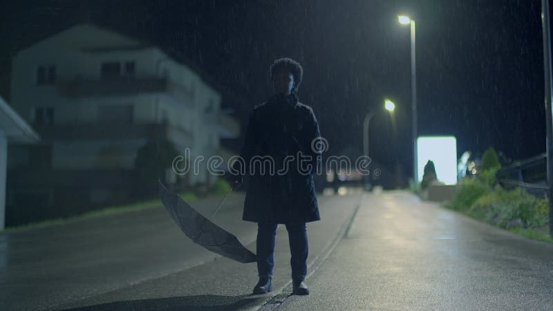 在雨中一条神秘的黑暗街道上，一把伞独自行走的人 股票录像