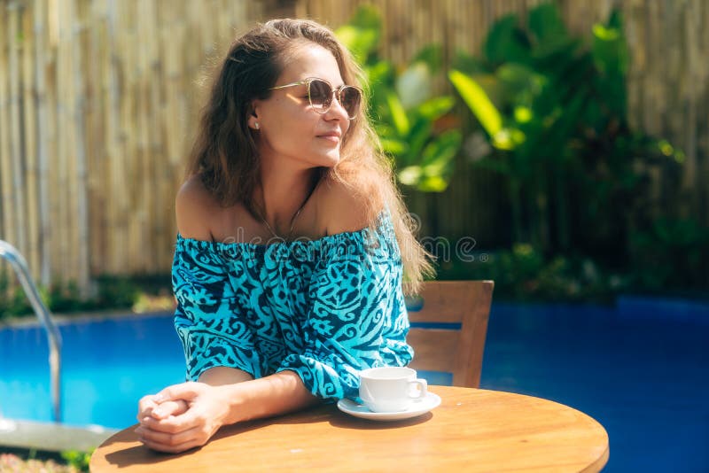 坐在与茶的桌上的太阳镜的美丽的被晒黑的女孩或咖啡 享受好日子的年轻女人 免版税库存图片 坐在与茶的桌上的太阳镜的美丽的被晒黑的女孩或咖啡 享受好日子的年轻女人 免版税库存图片