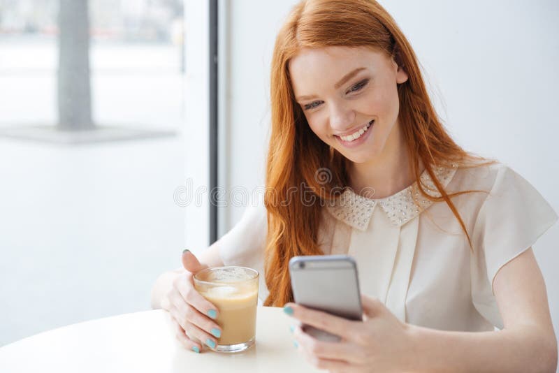 坐在咖啡馆和使用的微笑的妇女手机