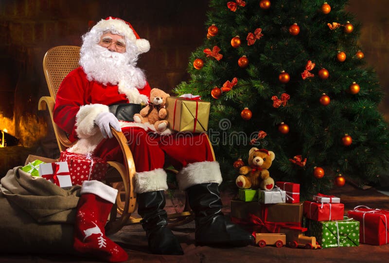 Santa Claus sitting in front of fireplace near Christmas tree with a bag full of presents and a wish list. Santa Claus sitting in front of fireplace near Christmas tree with a bag full of presents and a wish list