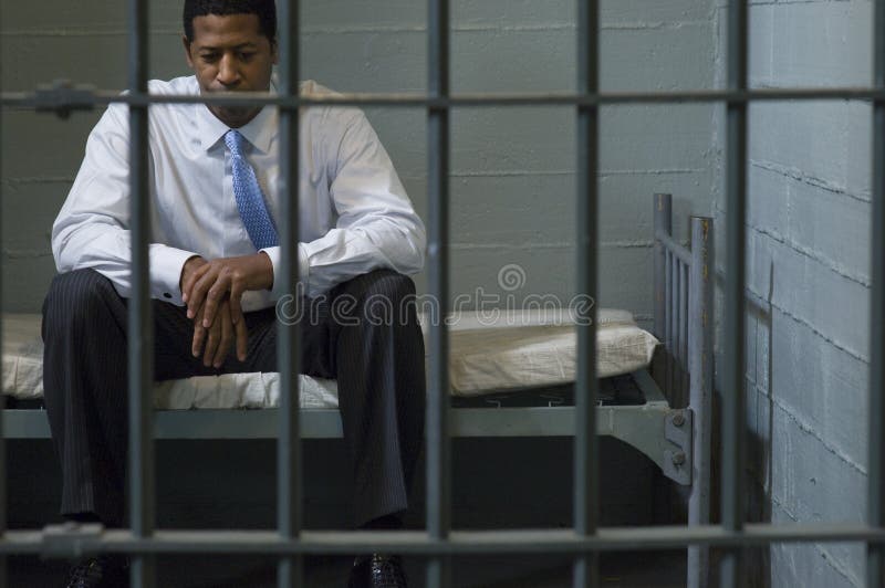 Depressed businessman sitting on bed behind prison bars. Depressed businessman sitting on bed behind prison bars