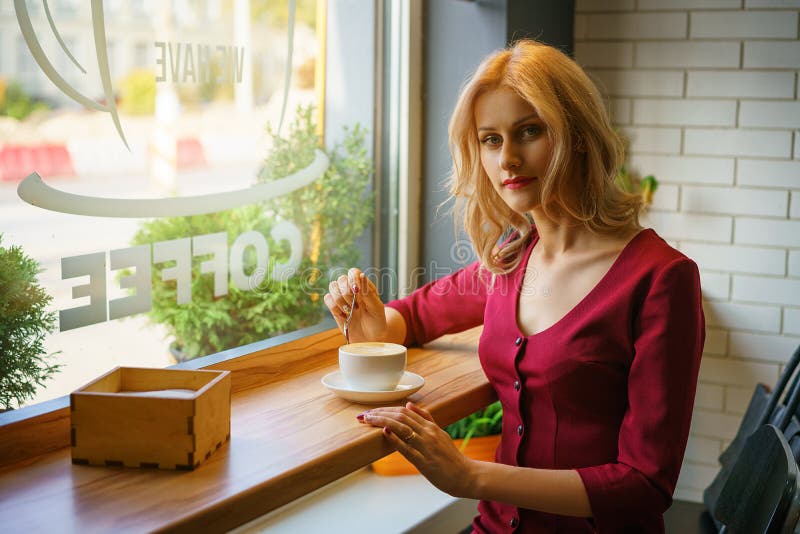 坐由在咖啡馆饮用的咖啡的窗口的美女 库存照片