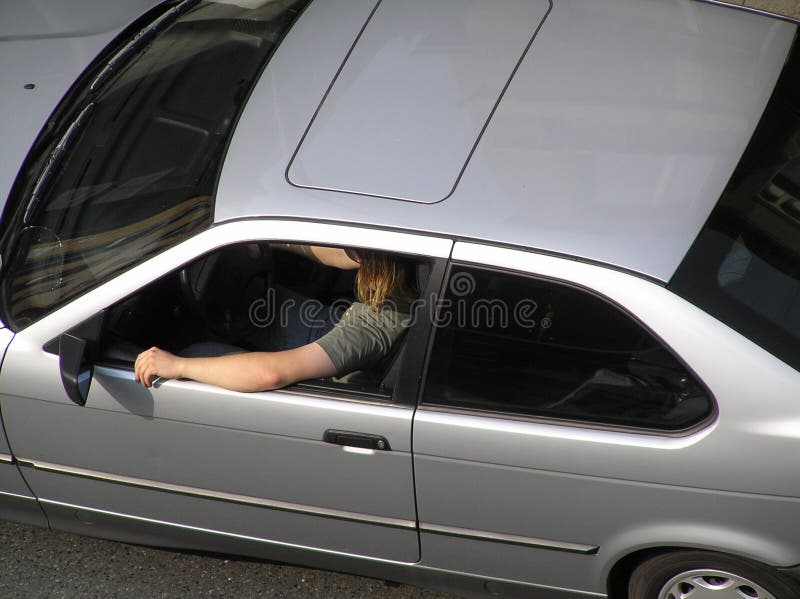 Young man with long hair drives a silver 2-door car. Young man with long hair drives a silver 2-door car.