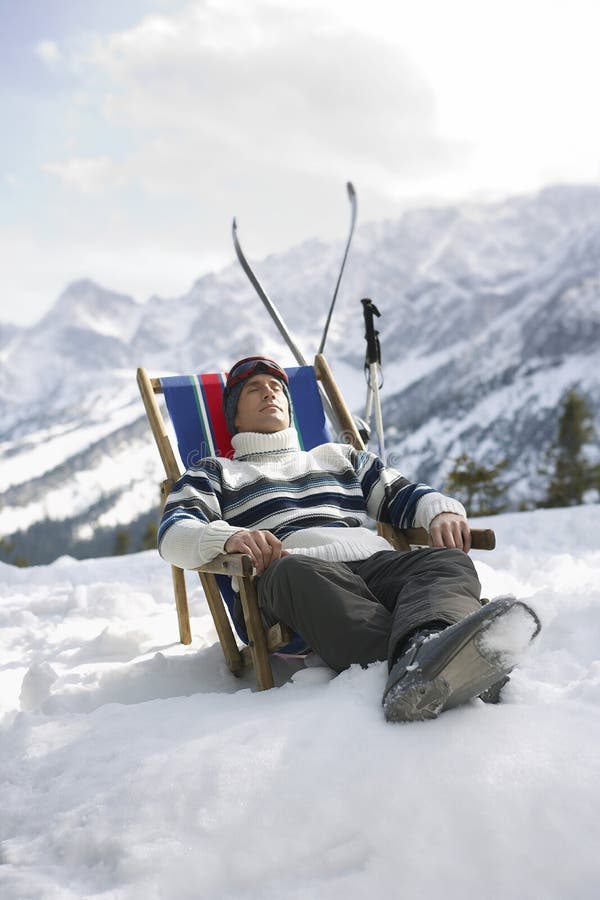 Man in warm clothing resting on deckchair in snowy mountains. Man in warm clothing resting on deckchair in snowy mountains