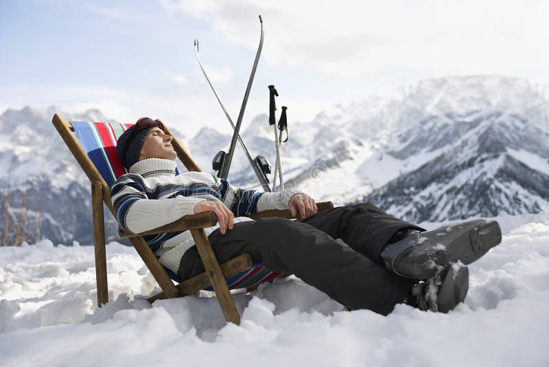 Side view of a man in warm clothing resting on deckchair in snowy mountains. Side view of a man in warm clothing resting on deckchair in snowy mountains