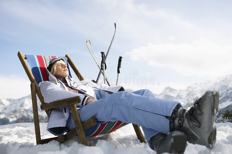 Side view of a woman resting on deckchair in snowy mountains. Side view of a woman resting on deckchair in snowy mountains