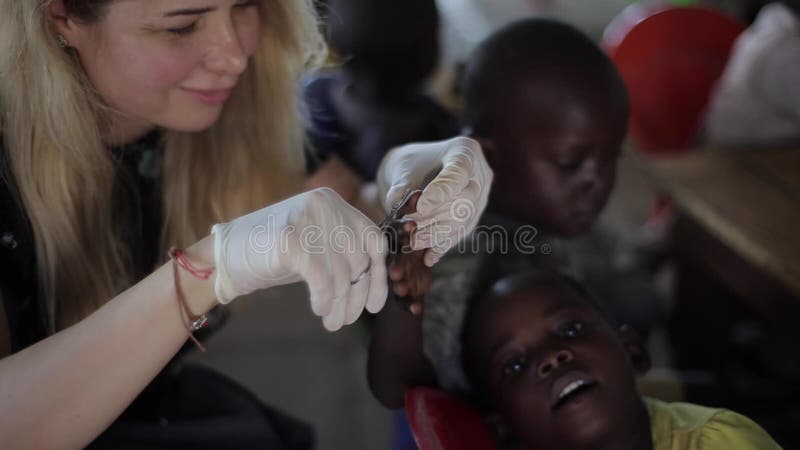 基苏木，肯尼亚- 2018年5月24日：白种人从非洲的妇女帮助的孩子 切开他们的与剪刀的女性钉子