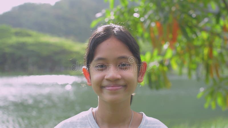 夏天，站在公园美丽的湖边，面带微笑、面带相机的可爱亚洲少女. 股票录像