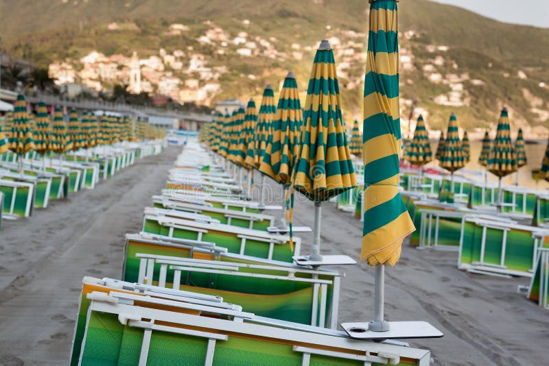 Many closed sun umbrellas and deckchairs on the sandy beach of the resort in summer. Many closed sun umbrellas and deckchairs on the sandy beach of the resort in summer.