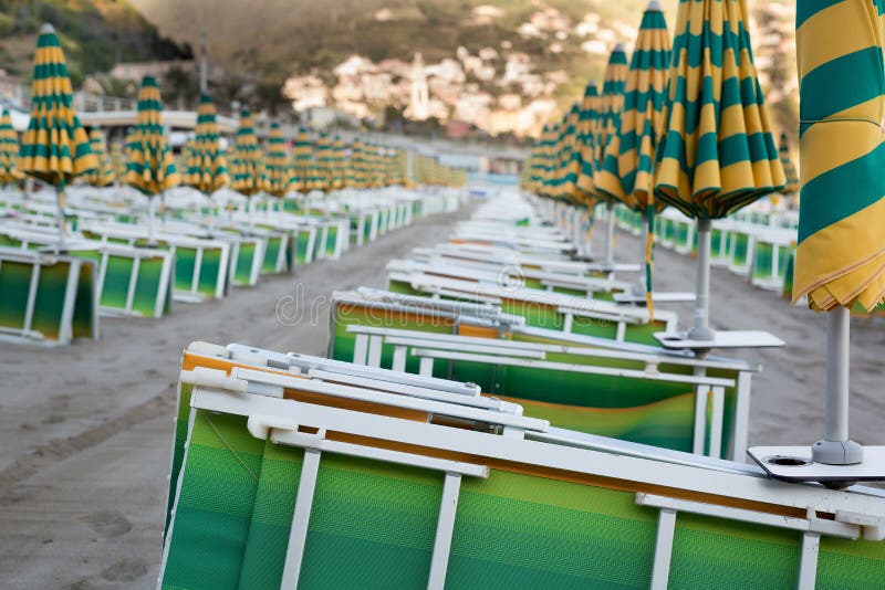 Many closed sun umbrellas and deckchairs on the sandy beach of the resort in summer. Many closed sun umbrellas and deckchairs on the sandy beach of the resort in summer.