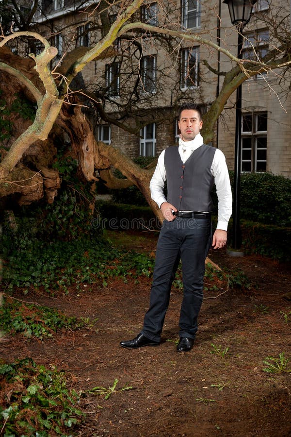 Man in Victorian Clothing in the park in front of a house and trunks of trees. Man in Victorian Clothing in the park in front of a house and trunks of trees