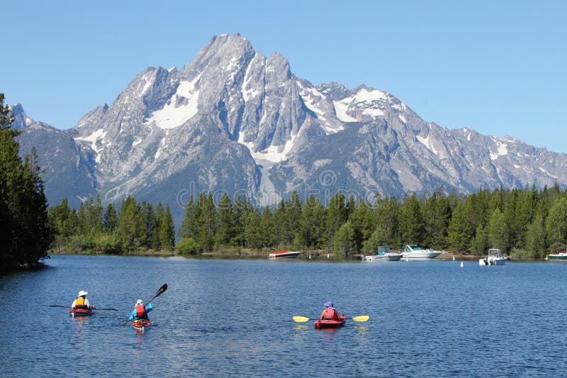 A group of three tourists floating in sea kyaaks on Jackson Lake in Grand Teton National Park, at the base of Mount Moran. A group of three tourists floating in sea kyaaks on Jackson Lake in Grand Teton National Park, at the base of Mount Moran