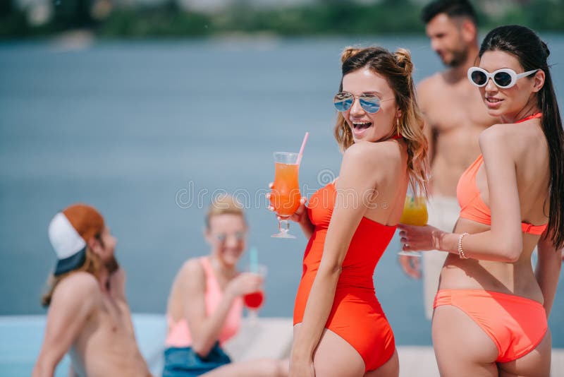 太阳镜的拿着鸡尾酒和微笑对照相机的美女和游泳衣 库存图片 太阳镜的拿着鸡尾酒和微笑对照相机的美女和游泳衣 库存图片