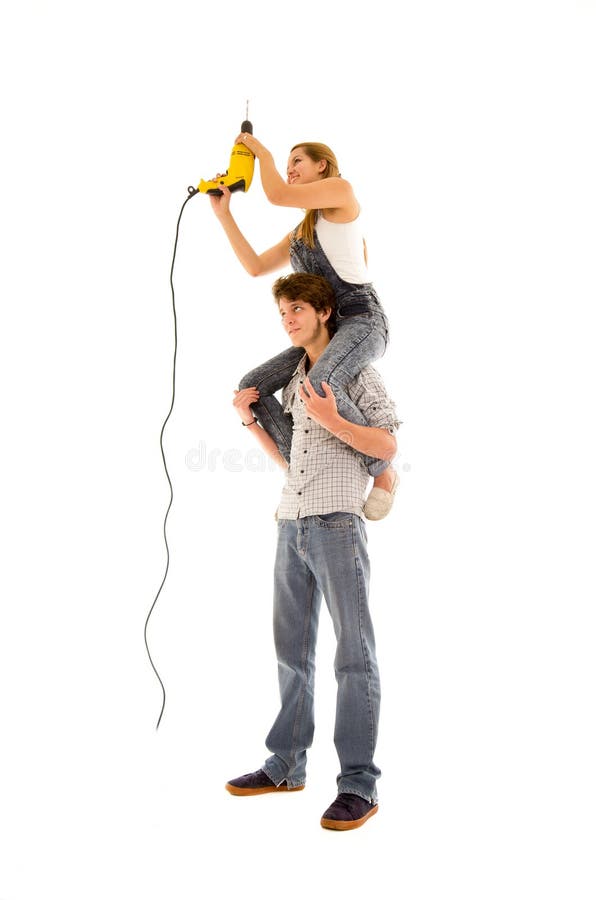 Couple wearing denim working with renovation as women sitting on mans shoulders and holding up a power drill, shot from side angle. Couple wearing denim working with renovation as women sitting on mans shoulders and holding up a power drill, shot from side angle.