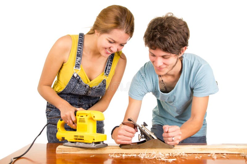 Couple standing by working desk as women uses electric sander and men holding a manual version. Couple standing by working desk as women uses electric sander and men holding a manual version.