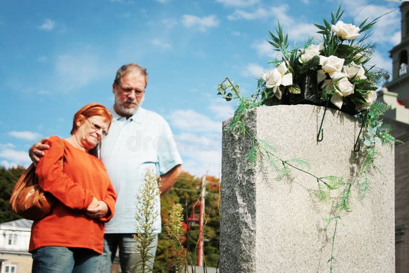 Couple praying in front of flowered tomb, in a cemetery. Couple praying in front of flowered tomb, in a cemetery