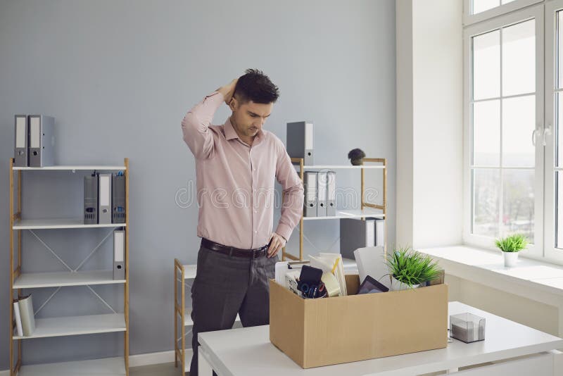 Unemployment. Dismissal. Dismissed businessman is upset with a cardboard box holding his head in his hands while sitting at a table in the company office. Stress failure Depression crisis problems without work. Unemployment. Dismissal. Dismissed businessman is upset with a cardboard box holding his head in his hands while sitting at a table in the company office. Stress failure Depression crisis problems without work.