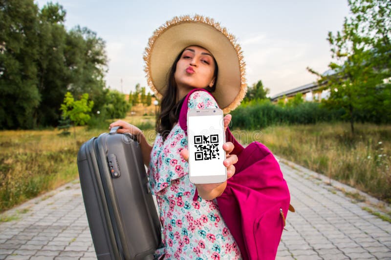 Beautiful woman is showing het phone with a QR code that she is vaccinated and is passing the border. She carried her backpack and luggage carry on. She is in the middle of a road. She is dressed in pink clothes and has a big summer hat. Beautiful woman is showing het phone with a QR code that she is vaccinated and is passing the border. She carried her backpack and luggage carry on. She is in the middle of a road. She is dressed in pink clothes and has a big summer hat.