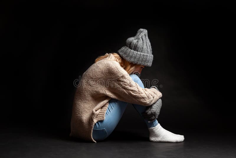 女孩单独坐在被接受她的腿用她的手的空虚黑背景的地板和投下她 库存图片 女孩单独坐在被接受她的腿用她的手的空虚黑背景的地板和投下她 库存图片