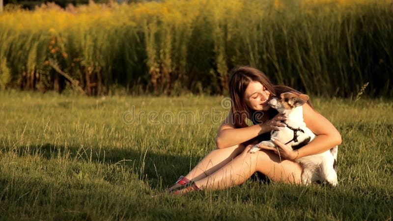 女孩坐草坪在公园并且亲吻她的狗