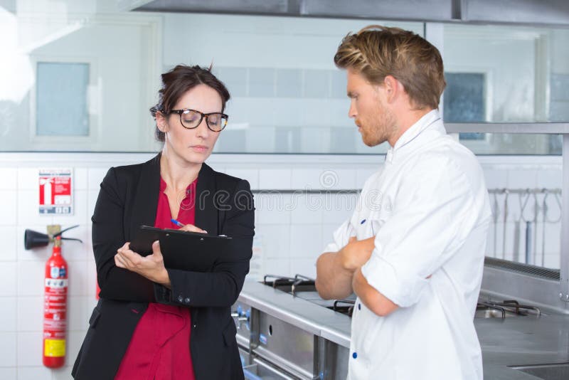 女检查员在餐厅厨房与厨师在一起 库存图片
