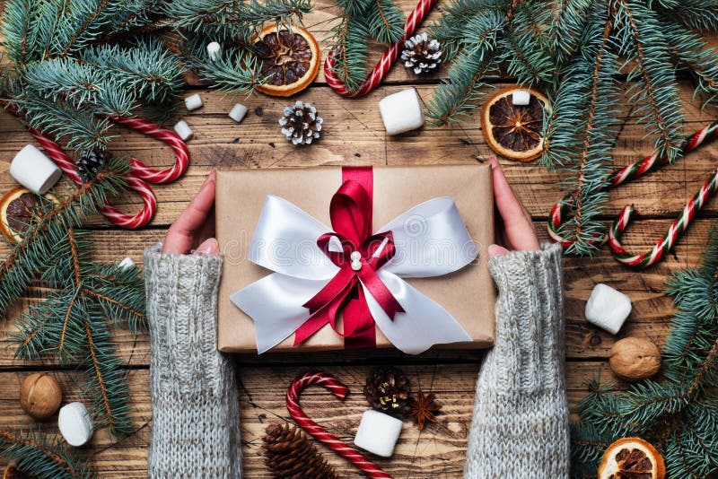 女手抱弓形礼盒 圣诞树和装饰、甘蔗焦糖和橙子坚果木质背景