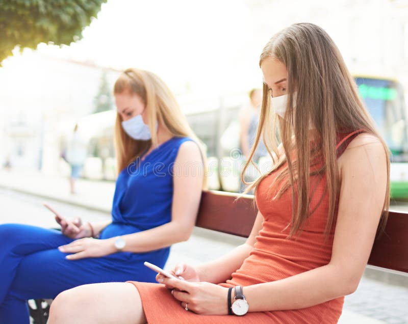 女朋友戴口罩使用智能手机年轻千禧一代查看社交媒体网络的更新新常态 免版税库存图片