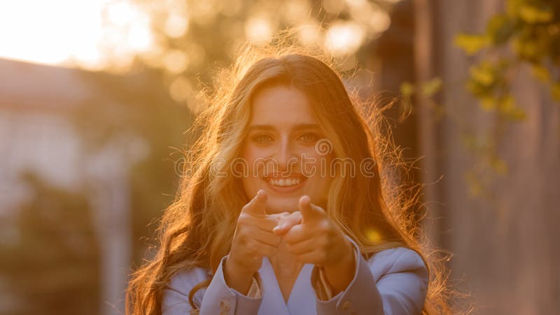 Portrait of female model stands on street in sunlight sunset happy smiling woman girl looking at camera makes gesture hey you hands pistols points index fingers direction agreeing pretending shooting. High quality photo. Portrait of female model stands on street in sunlight sunset happy smiling woman girl looking at camera makes gesture hey you hands pistols points index fingers direction agreeing pretending shooting. High quality photo