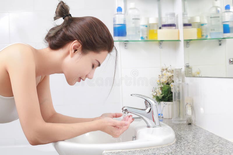 Woman washing her face with water above bathroom sink. Woman washing her face with water above bathroom sink