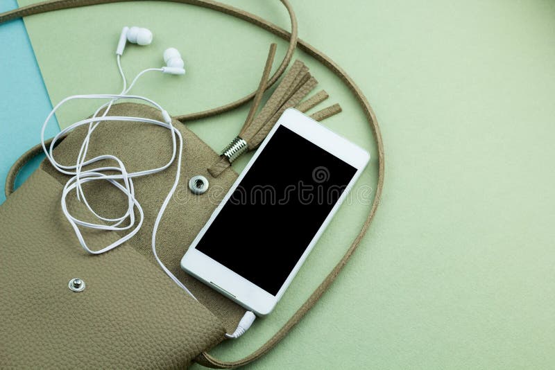 Top view contents of women bag phone mock up black screen and earphones in an open bag on the green and blue background. Top view contents of women bag phone mock up black screen and earphones in an open bag on the green and blue background