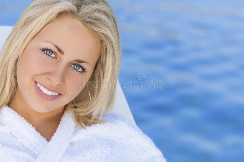 Beautiful blonde girl young woman in white spa robe with natural blue water background. Beautiful blonde girl young woman in white spa robe with natural blue water background