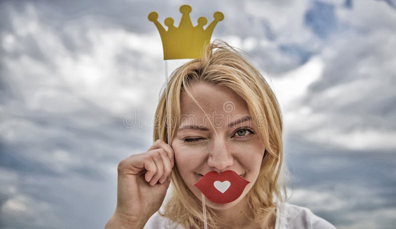 嬉戏的公主 妇女金发举行纸板冠状头饰或冠和爱天空背景的红色嘴唇标志 ?? 免版税库存照片 嬉戏的公主 妇女金发举行纸板冠状头饰或冠和爱天空背景的红色嘴唇标志 ?? 免版税库存照片