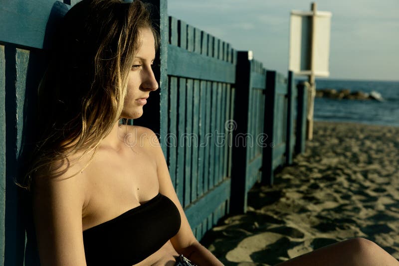 孤独的哀伤的年轻白肤金发的在海滩的妇女沉思开会在日落 免版税库存图片