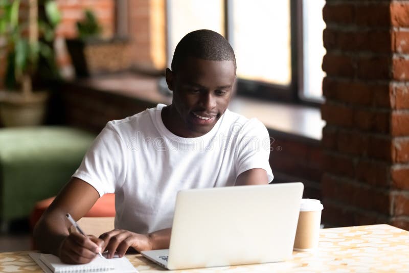 学习在膝上型计算机的微笑的黑男性做在笔记本的笔记