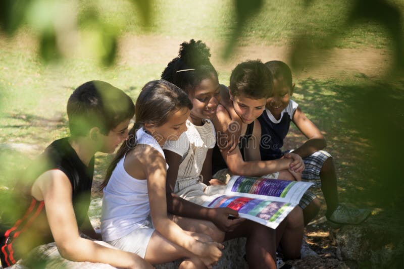 Young people and education, two little girls and boys reading book in city park. Young people and education, two little girls and boys reading book in city park