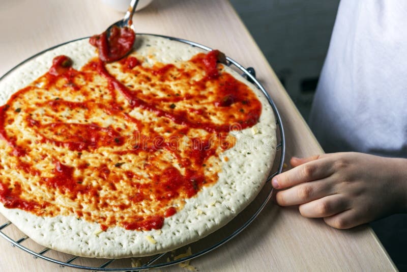 孩子把酱汁撒在披萨面团上 儿童自制比萨的烹饪方法 学前技能,小助手 家族 免版税库存照片 孩子把酱汁撒在披萨面团上 儿童自制比萨的烹饪方法 学前技能,小助手 家族 免版税库存照片