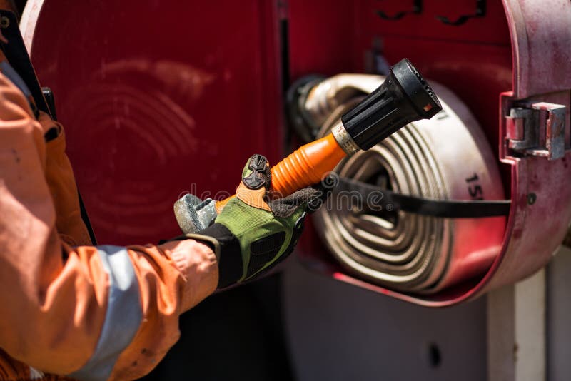 Man in safety gloves and orange coverall is taking fire nozzle from fire box. Man in safety gloves and orange coverall is taking fire nozzle from fire box.