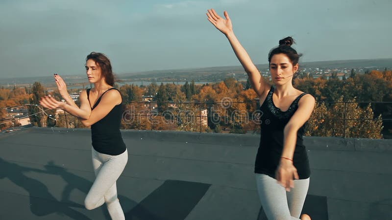 实践在屋顶的两名美丽的妇女瑜伽asana，户外在早晨